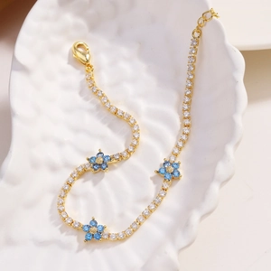 Close-up of golden flower bracelet with white and blue zircon stones on a white ceramic dish