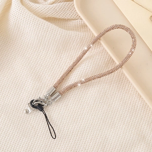 Detail of champagne gold rhinestone phone lanyard with silver metal clasp on beige fabric