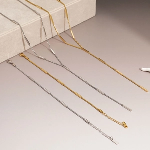 Minimalist stainless steel necklaces in gold and silver finish on a beige jewelry box