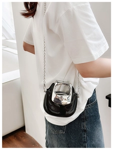 Detail of mini black patent leather bucket bag with silver handle worn cross-body