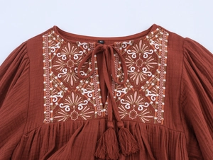 Detail of bohemian rust red blouse with intricate embroidery and tassel neck tie