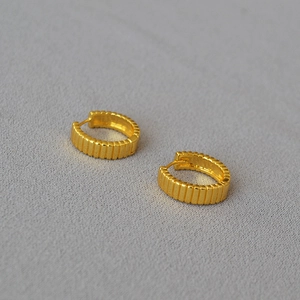 Dettaglio di orecchini a cerchio placcati oro con texture a costine e righe verticali