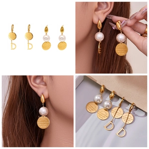 Détail des boucles d'oreilles médaillon dorées 18K avec perles et pendentif lettre D