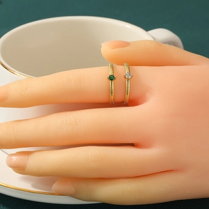 Minimalist gold rings with green and clear gemstones worn on hand, textured band design