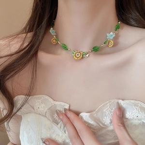 Detail of sunflower necklace with enamel pendants and green beads on a white lace dress