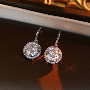 Close-up of silver hoop earrings with a large central zircon and halo setting in soft light
