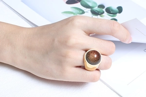 Detailed view of chunky gold ring with large brown sandstone on model holding a catalog
