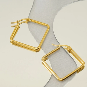 Detailed view of square gold earrings on a reflective mirror with gray ribbon