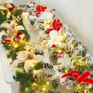 Christmas garland with flocking, LED lights, red bows and pine cones on a white table
