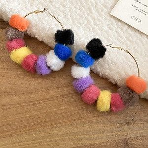 Detail of colorful pompom hoop earrings on soft white fleece and light wood background