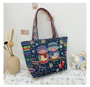 Detailed embroidery of two colorful owls and snowflakes on a navy canvas tote bag