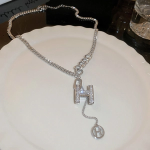 Macro detail of silver H-letter necklace with pavé crystal settings on ceramic plate