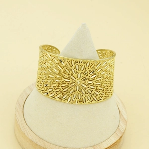 Detailed macro view of wide gold cuff bracelet with intricate hollow floral patterns