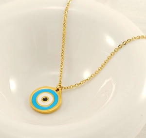Detailed close-up of a golden Evil Eye pendant on a chain inside a white ceramic bowl