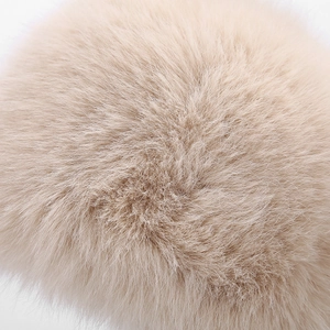 Close-up of soft fluffy beige faux rabbit fur pom-pom with dense plush texture and shine