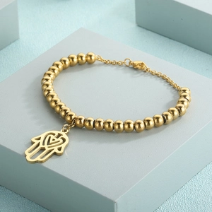 Macro detail of a golden beaded bracelet featuring a hollow Hamsa hand pendant and lobster clasp