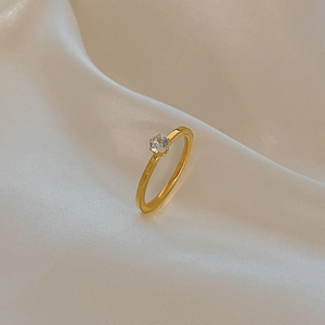 Detail of a minimalist gold ring with six-prong set cubic zirconia on white silk cloth