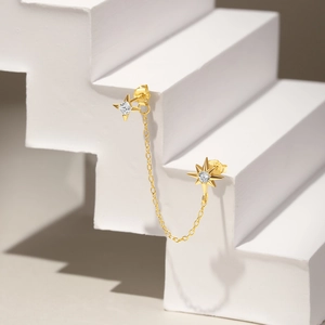 Detail of gold chain earrings with star charms and white cubic zirconia on white steps