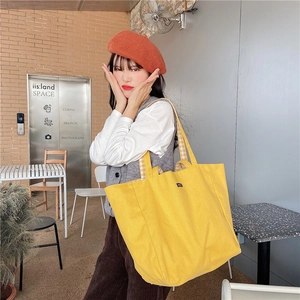 Detailed view of yellow canvas tote bag with plaid handles shown in a lifestyle cafe setting