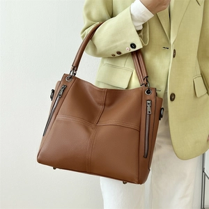 Brown leather tote bag with decorative side zippers and dual handle shown on a model