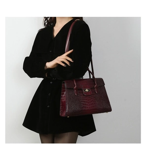 Detail of burgundy crocodile pattern handbag with gold twist lock shown on a model