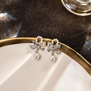 Elegant silver bow earrings with sparkling crystals and hanging pearls on ceramic