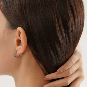 Gros plan d'une boucle d'oreille cœur argentée sur un modèle, design épuré en acier