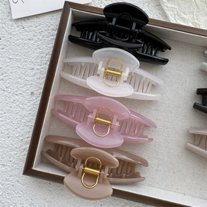 Detail of four matte pastel hair claws with gold springs in a wooden tray