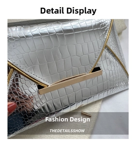 Detail of silver envelope clutch featuring crocodile embossed texture and golden metal hardware