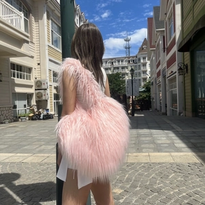 Outdoor shot of a large heart-shaped pink faux fur crossbody bag worn by a model