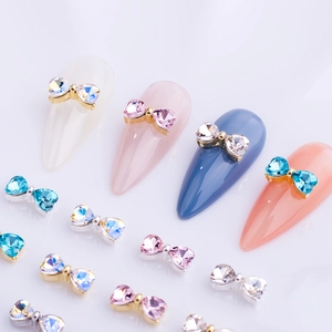 Detailed view of colorful bow-shaped nail charms with crystals on various nail tips