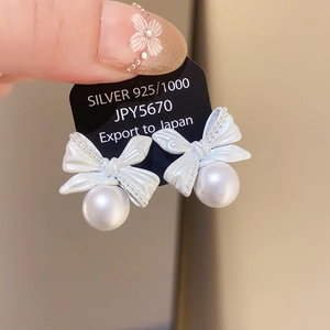 Close-up of 925 silver bow earrings featuring elegant white pearls and delicate textures
