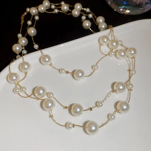 Detail view of multi-layer faux pearl necklace with gold chain on white ceramic plate