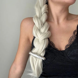 Macro detail of a silver hammered metal hair clip styled on a golden braided ponytail