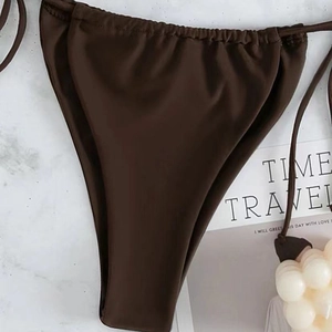 Detail view of dark coffee bikini bottoms with side drawstrings on marble surface