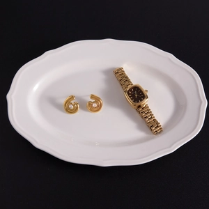 Détail de boucles d'oreilles 18K avec zircon et montre carrée sur un plateau en porcelaine