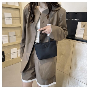 Sac seau chic en nylon noir présenté avec un ensemble tailleur kaki minimaliste