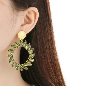Vintage oversized gold hoop earrings with green glass leaf charms worn by a model