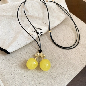 Detail of yellow cherry pendant with gold leaves on a minimalist black wax cord necklace