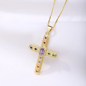 Macro detail of gold cross pendant with purple center stone and colorful gems on white fabric