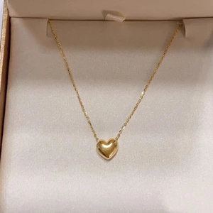 Detailed close-up of 18K gold heart necklace inside a minimalist beige jewelry box