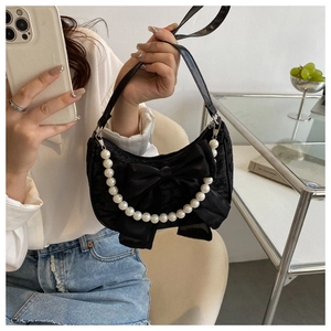 Detail of a chic black satin handbag with a large bow and pearl chain strap