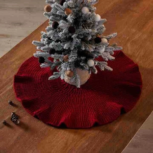 Burgundy knitted mini Christmas tree skirt with ruffled edge on dark wood tabletop