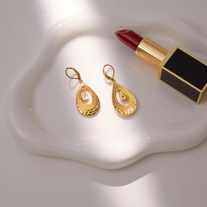 Gold stainless steel teardrop earrings with zircon on white ceramic tray