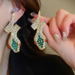 Vintage gold snake earrings with white diamonds and green stone accents on a person