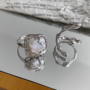 Baroque pearl ring and minimalist lava flow silver rings on a reflective surface