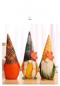 Close-up of three autumn harvest gnomes with maple leaves and plaid hats on wooden surface