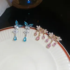 Eleganti orecchini a fiore con zirconi blu e rosa e nappine su un piatto bianco
