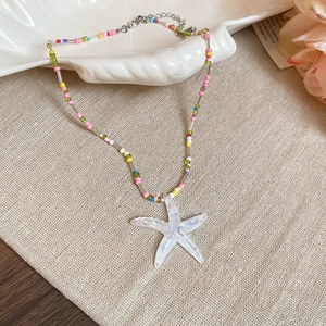 Detail of a colorful beaded necklace with a white glitter starfish pendant on a shell tray