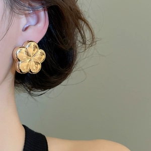 Close-up of polished gold flower stud earring on ear showing elegant 3D floral design